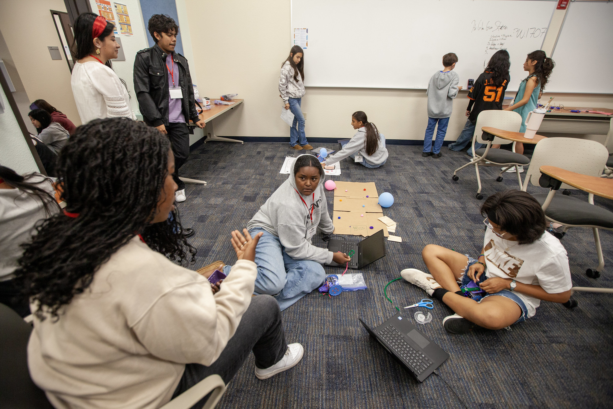 a group of students working on their robots, students decorating their robots and brainstorming ideas on a whiteboard in the background
