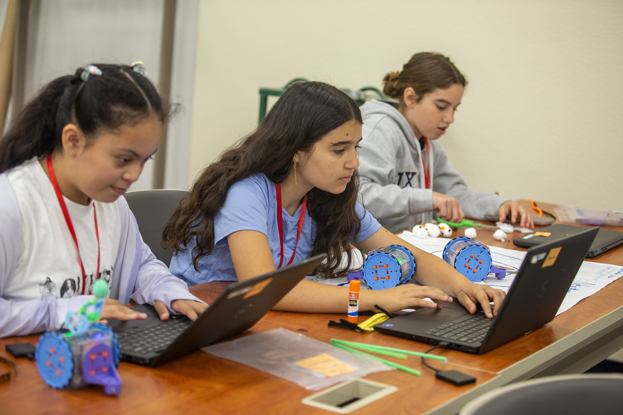3 students seated at a table, coding on their laptops
