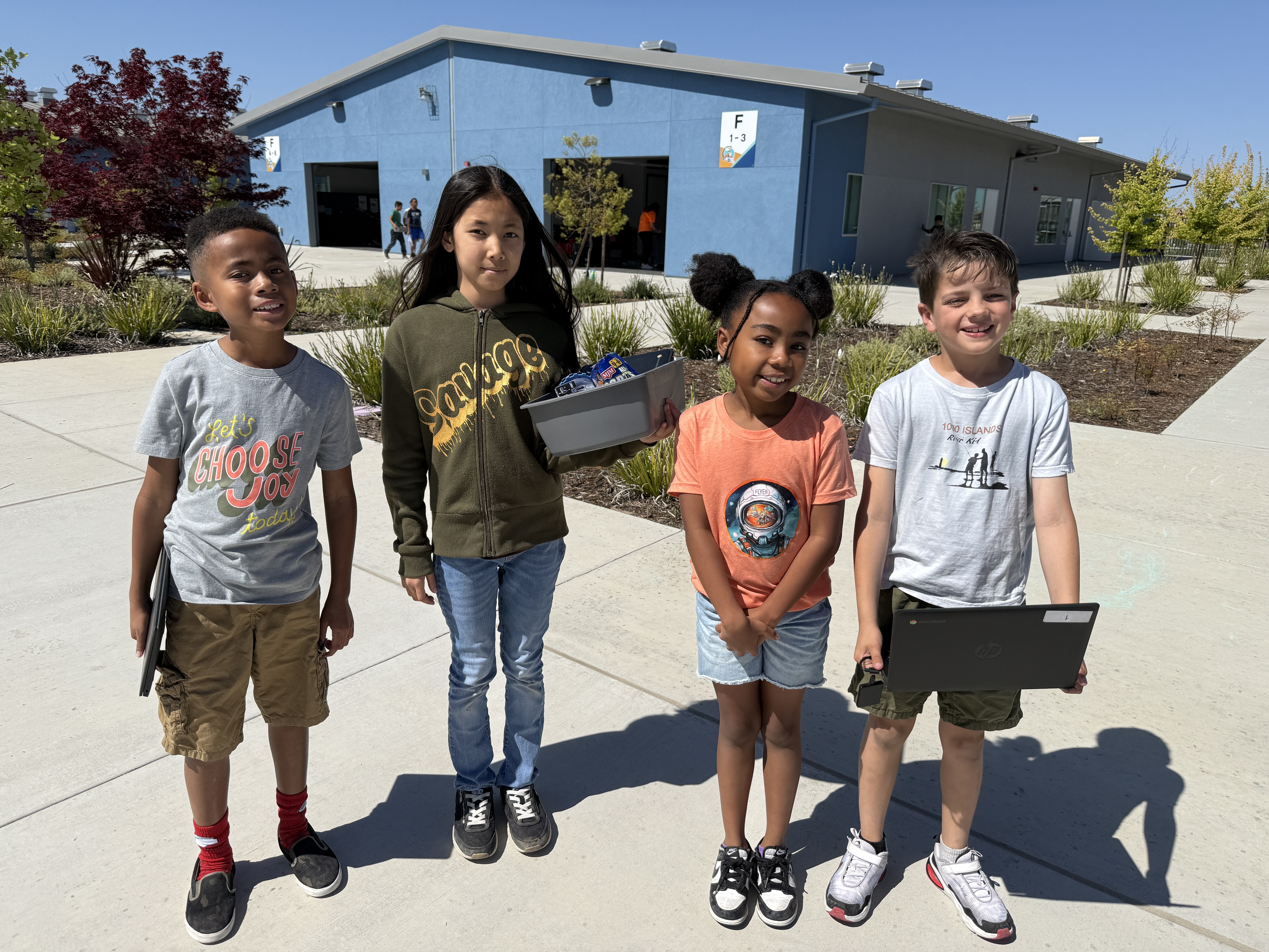 students standing in the sun carrying laptops and robots