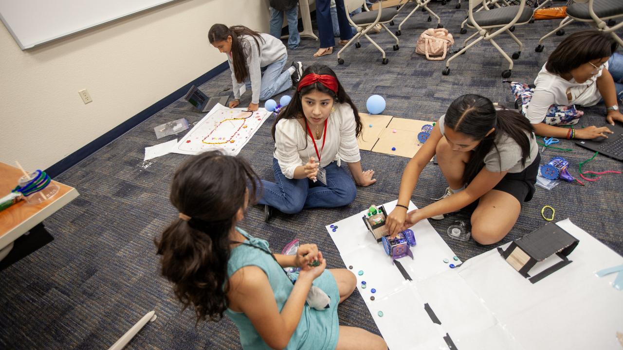 girl camp students on the floor programming a linkbot, other students coding in the background
