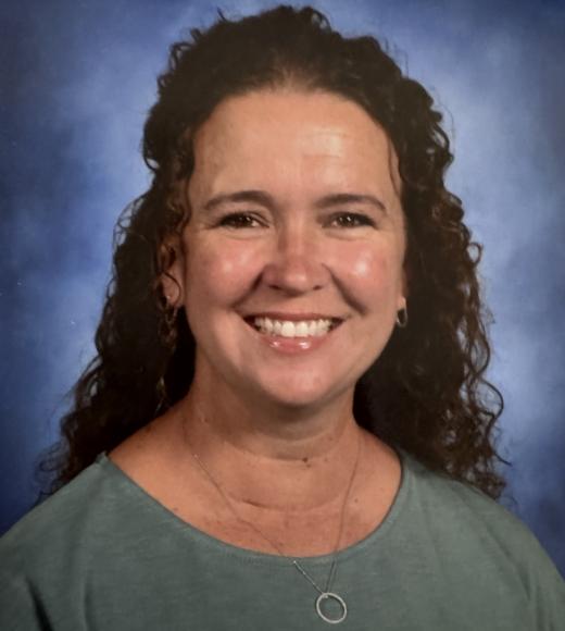School portrait of a smiling woman with curly dark hair, teal top, blue backdrop