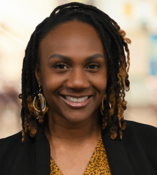 Headshot photograph of smiling Black woman with dreadlocks and hoop earrings.