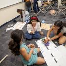 girl camp students on the floor programming a linkbot, other students coding in the background
